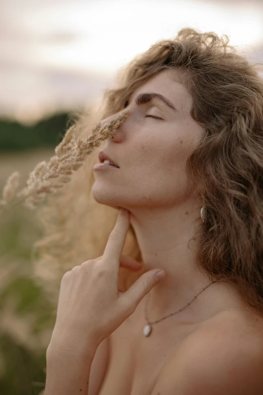 a woman standing with her eyes closed next to her hand near a flower