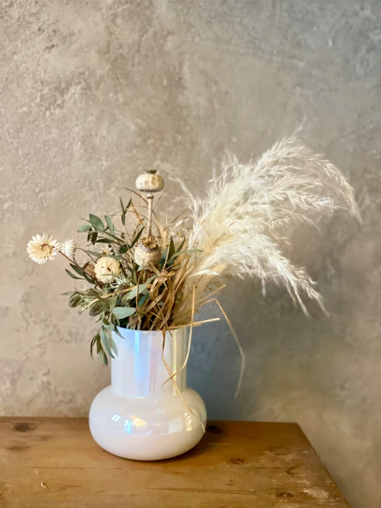 a white vase with dry flowers and feathers