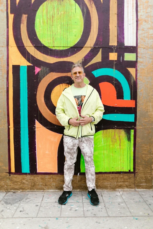 the man stands beside an abstract painting, which is also painted in yellow