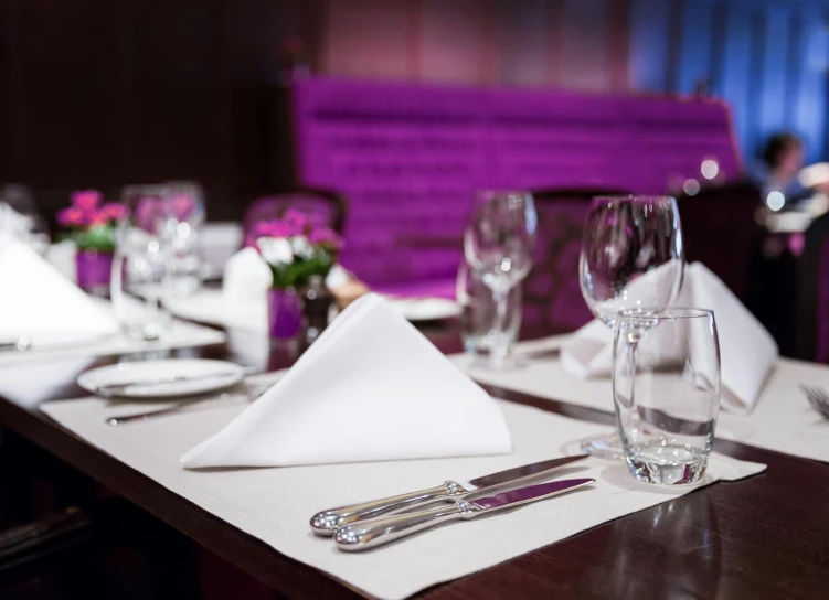 a dinner table set with glasses, napkins and place settings