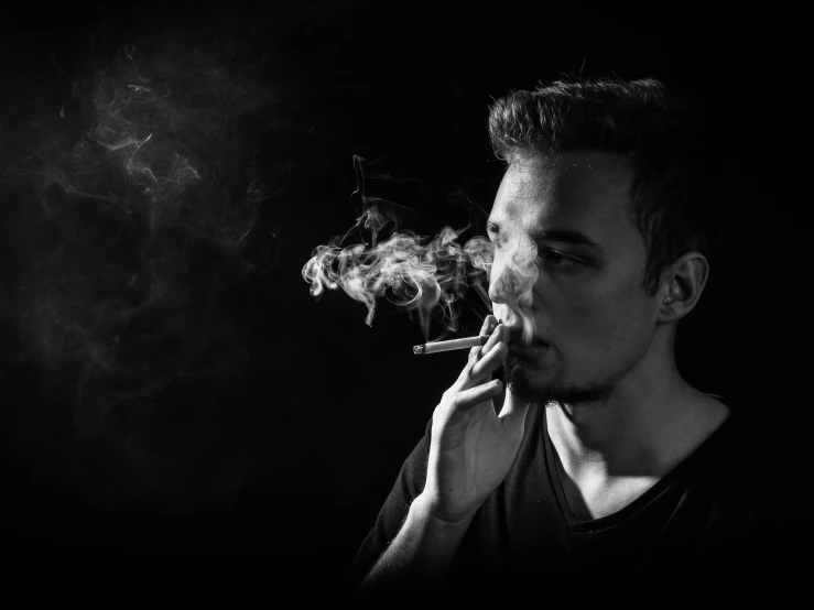 man with cigarette and black background smoke is coming out from his mouth