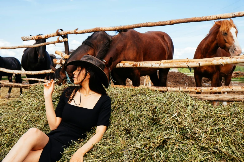 the woman in a hat sits in hay with horses