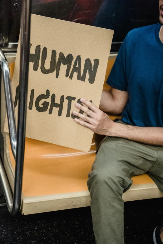 man sitting holding sign on subway seat during day