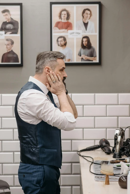 man with hands on face talking on a phone in a white tiled bathroom