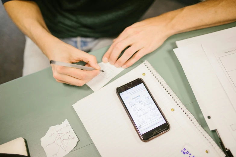 an image of someone writing on a piece of paper with a cell phone