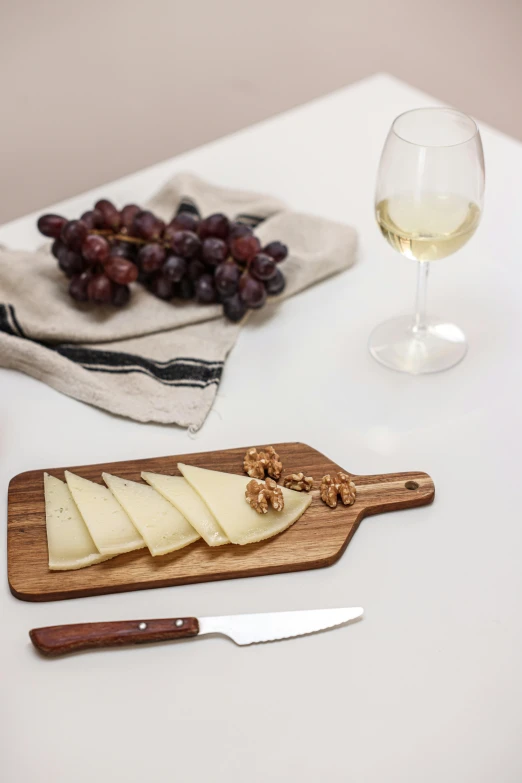 sliced up cheese sitting on top of a wooden  board next to a glass of wine