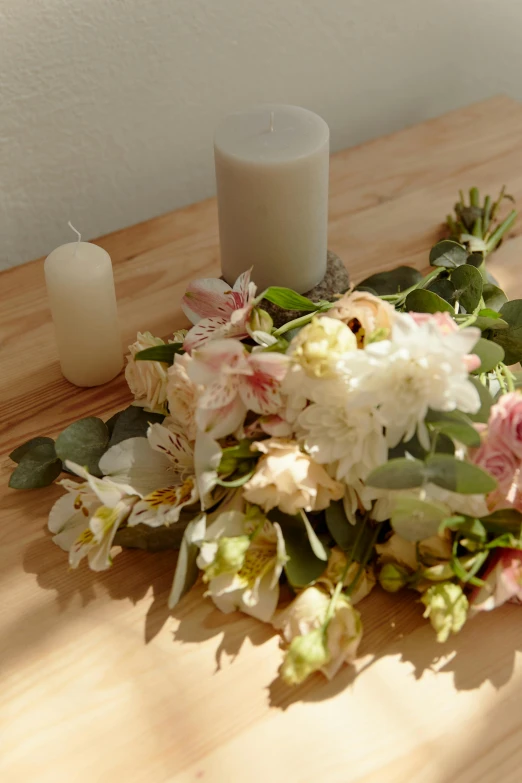 a bouquet of flowers and a white candle sit on a wooden table