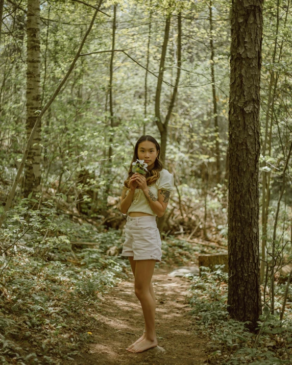 a woman in white clothes is standing in the woods holding a flower