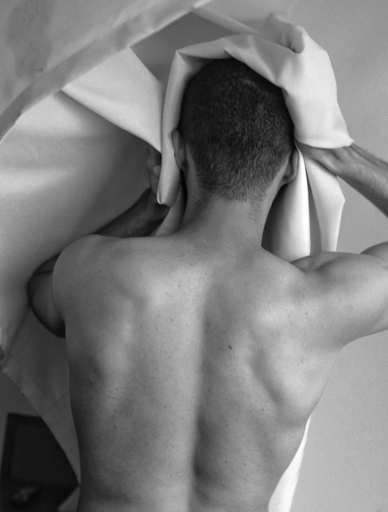 man with towel over his head looks at the wall