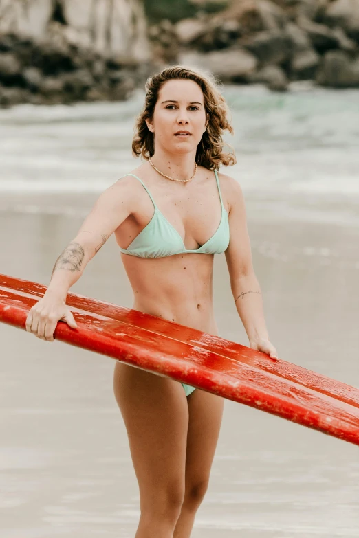 a woman is standing on the beach holding her surfboard