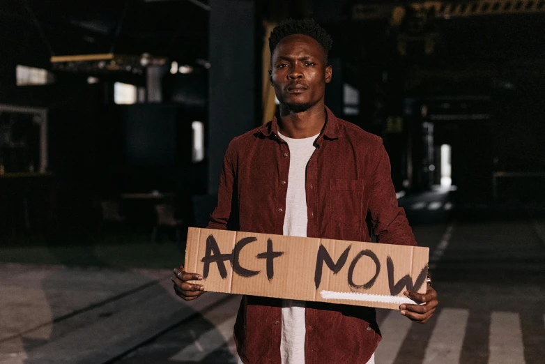a man standing next to a street holding a sign that says act now