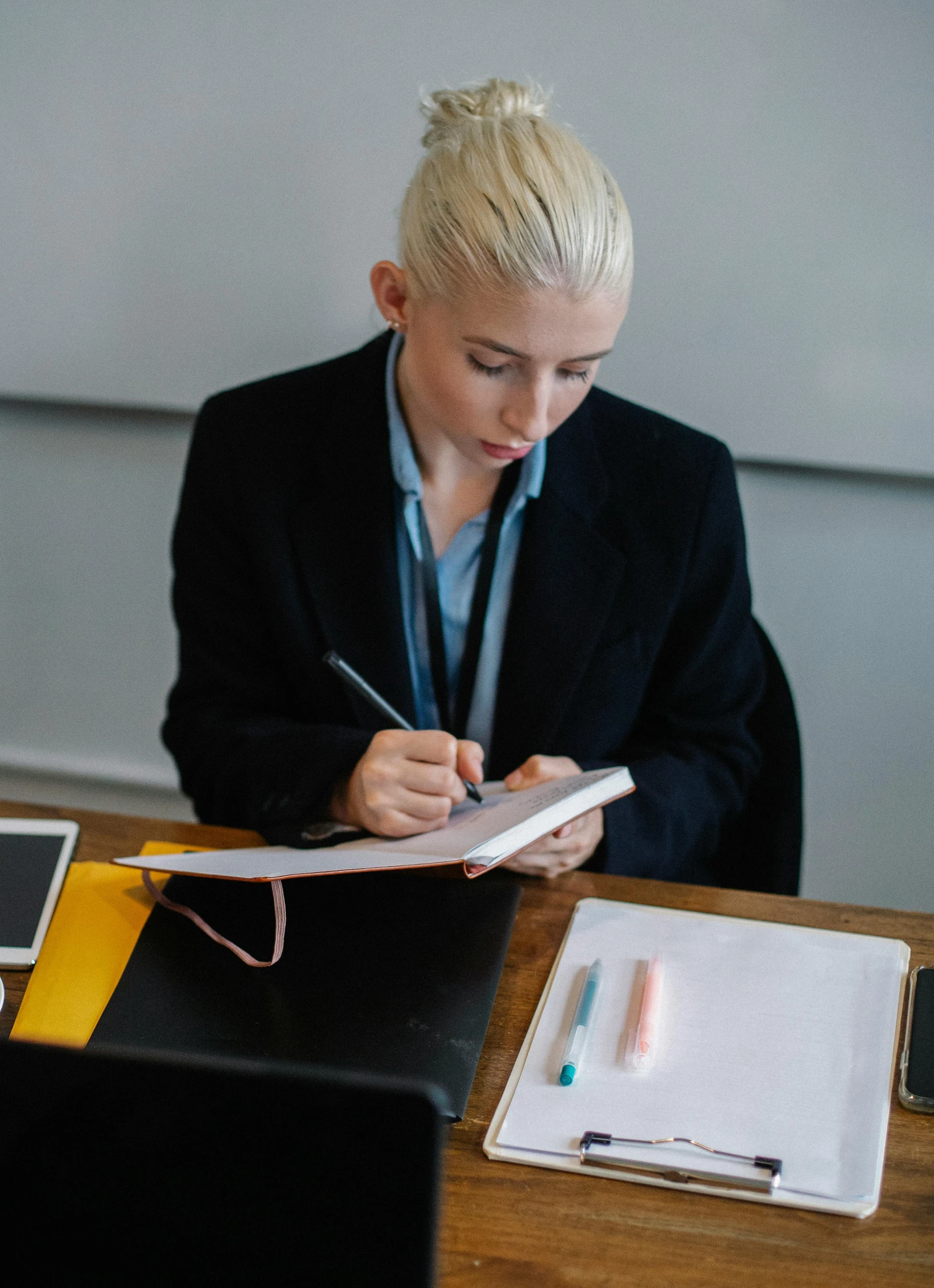 woman in business attire writing at desk with tablet