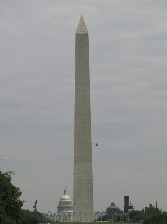 an obelisk stands in the distance behind an american flag