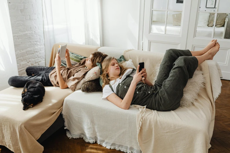 two girls are lying on a couch looking at a cell phone