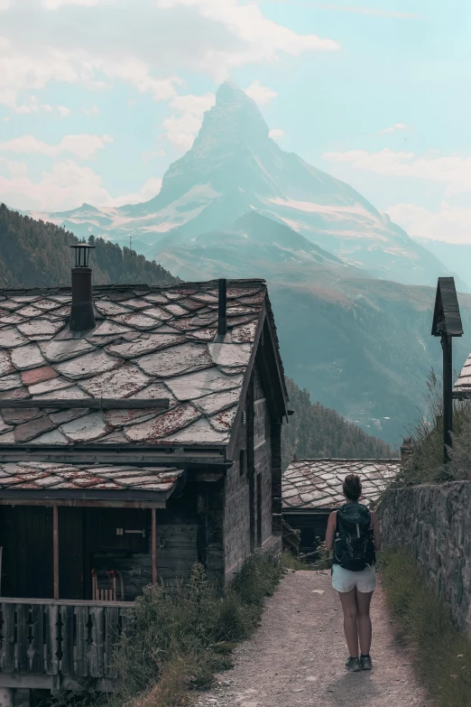 a woman is walking up the trail towards some houses and mountains