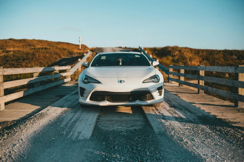 a white car on a road next to a wooden bridge