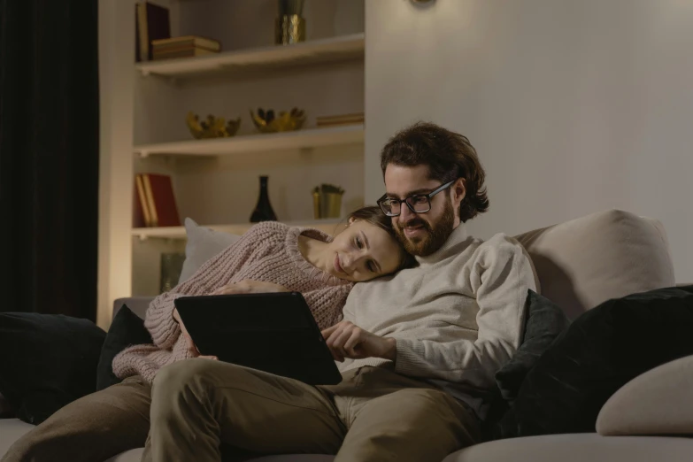 a man and woman laying on a couch looking at their laptop