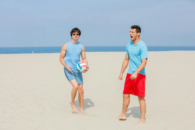 two men in the sand on a beach holding balls