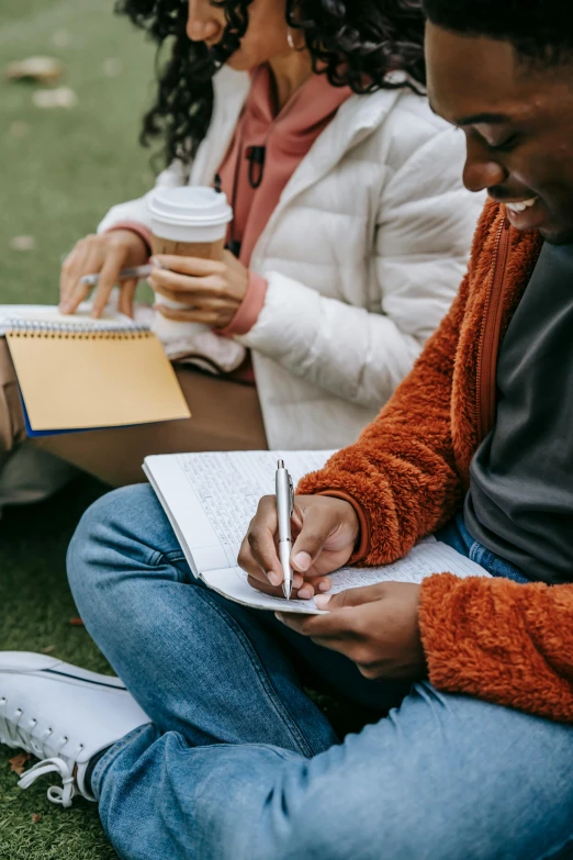 a man writing on a notebook while a woman sits beside him