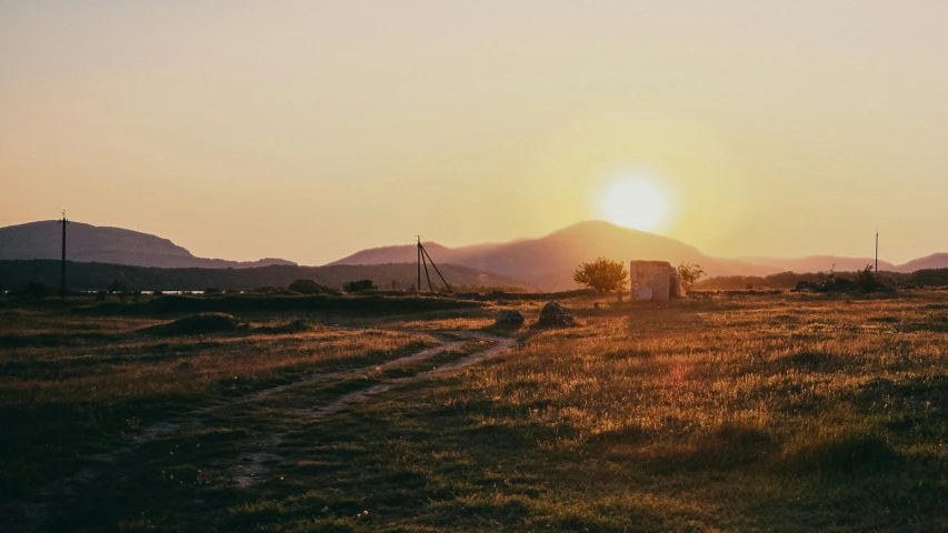 a dirt road in a field with hills on either side and one building