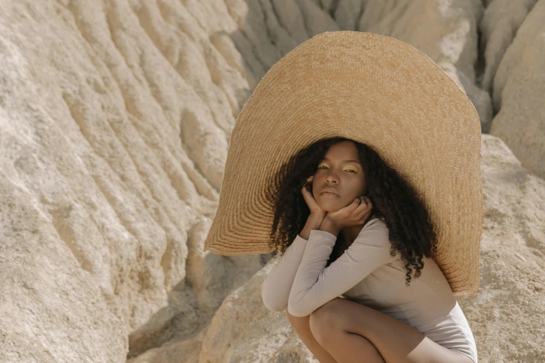 there is a woman sitting on a cliff with a large hat