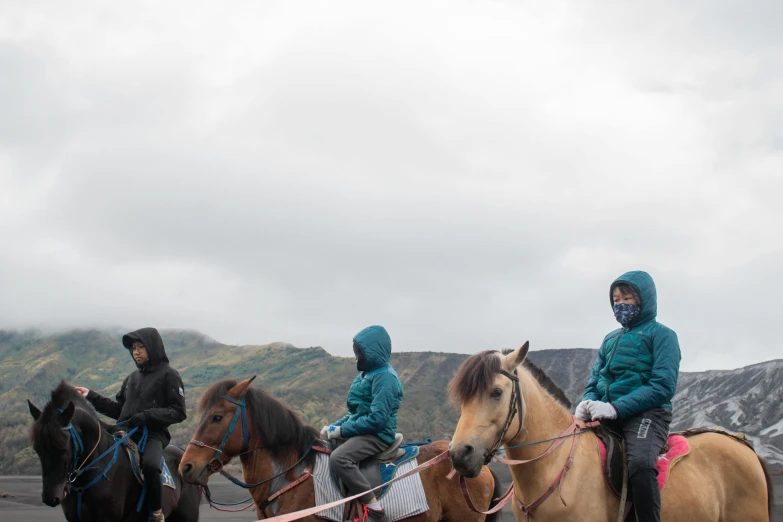 three young people riding horses in the mountains