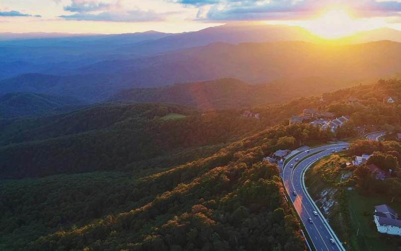 sun rises over the mountains behind road curving in front of a city