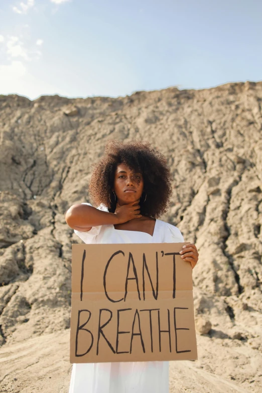 woman holding a cardboard sign reading i can't breathe