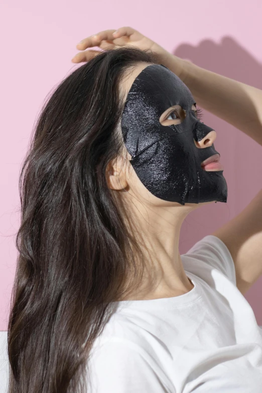 a woman is putting a black face mask on her face