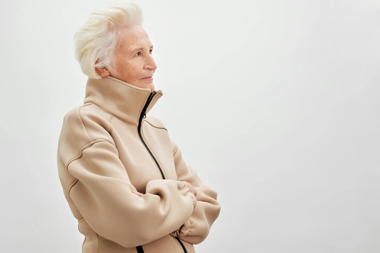 an elderly woman in a tan jacket standing with her arms folded