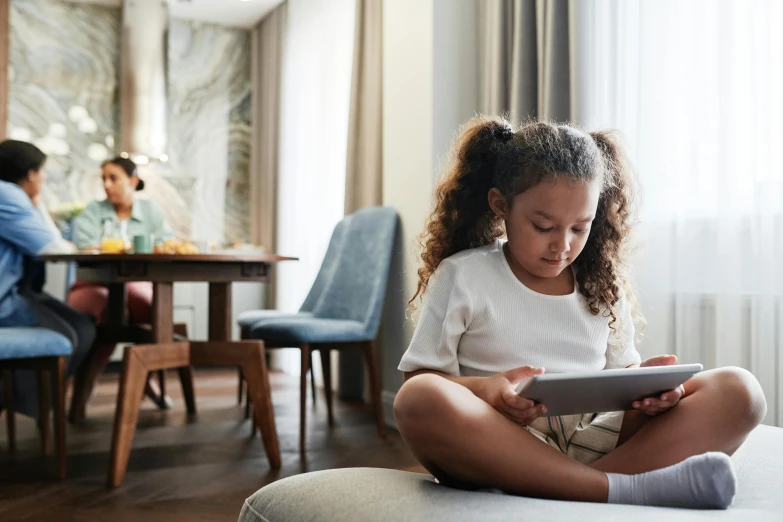 a little girl sitting on the floor and using a tablet computer