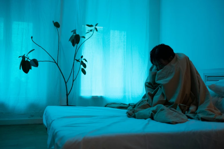 a dark room with curtains and a person wrapped in blankets sitting on the bed