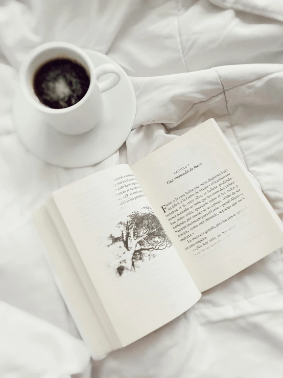 an open book and coffee sitting on top of a bed