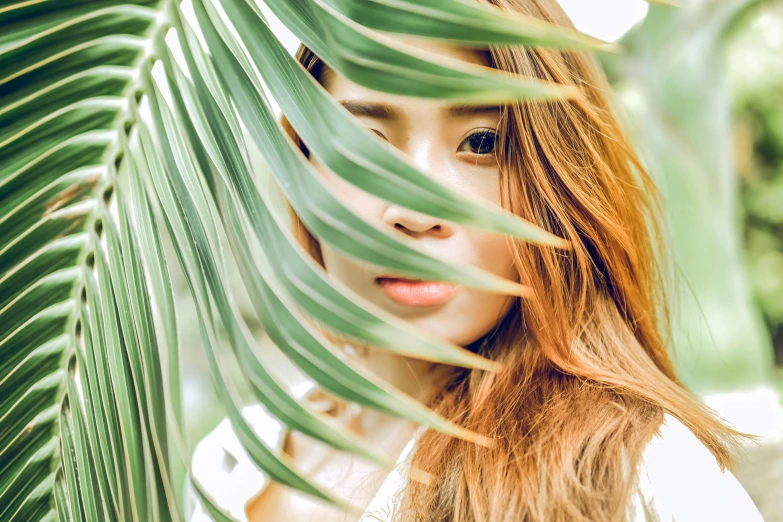  hiding her face behind tropical leaves