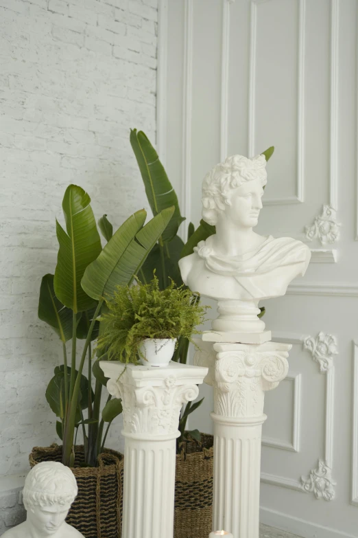 two white sculptures sit beside green plants and vases