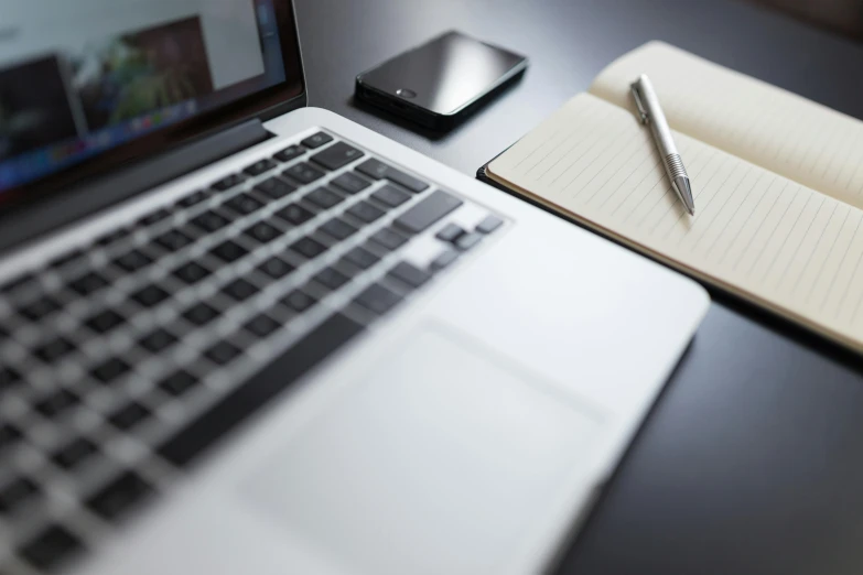 a black laptop computer with an open notebook and pen next to it