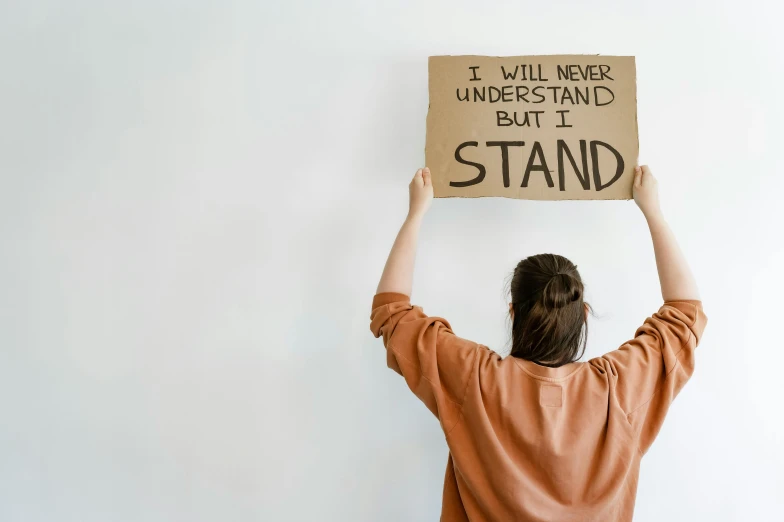 a young woman is holding up a cardboard sign with a message