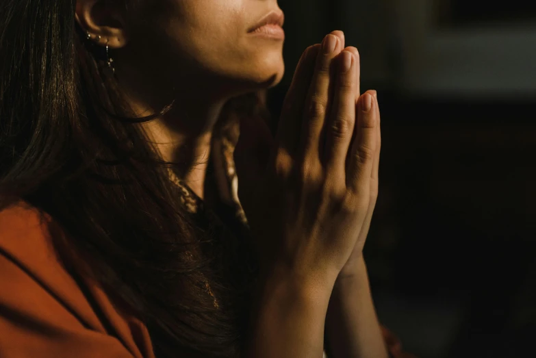 a woman in orange is praying with her hands clasped together