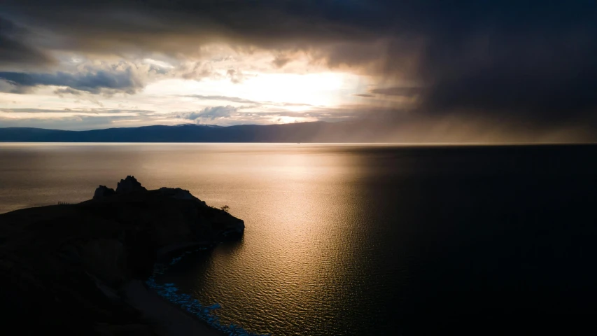 sun peeking through clouds over the ocean and cliff