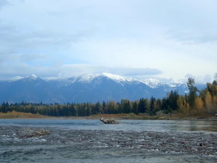 some mountains and snow are seen behind the water