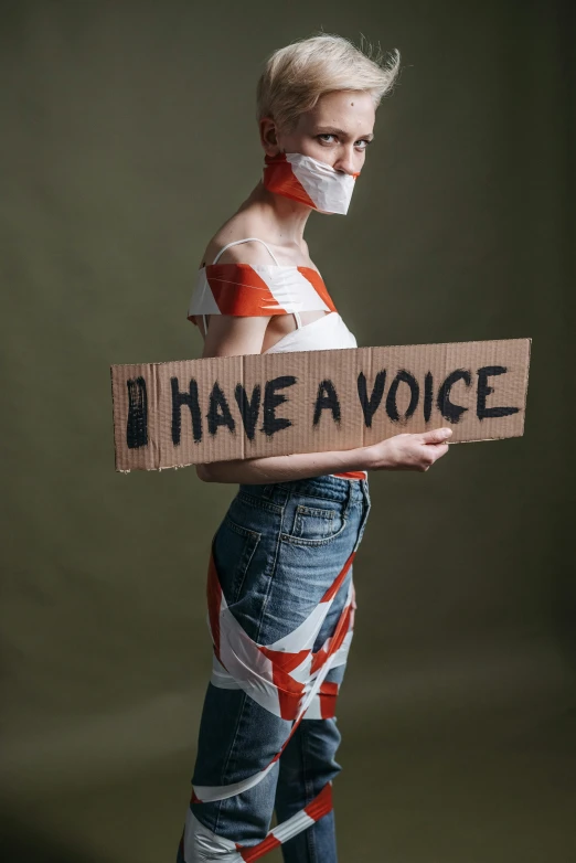 a woman in a white shirt is holding up a cardboard sign that reads i have a voice