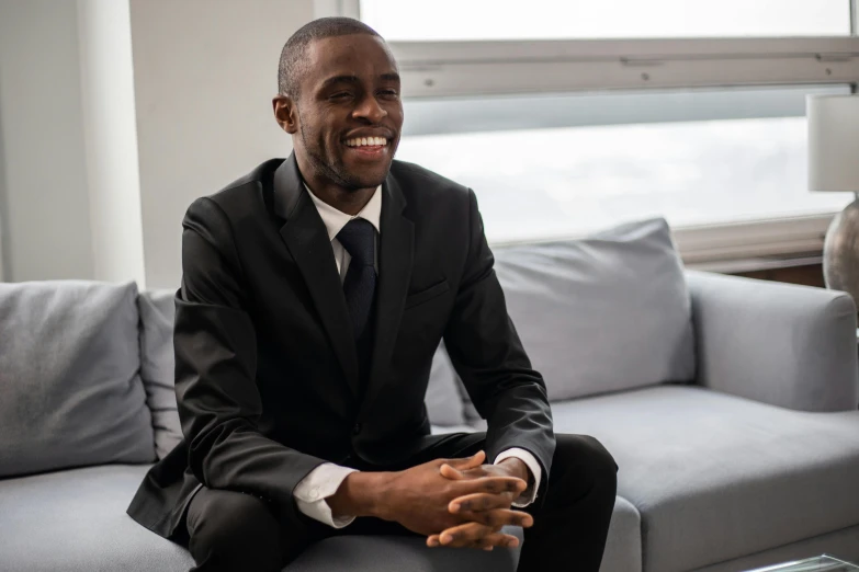 a smiling black man sitting on top of a grey couch