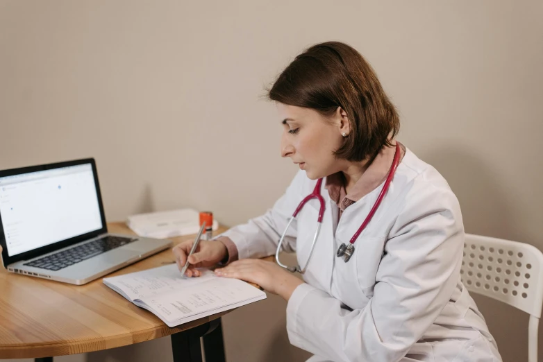 a woman with a white lab coat writing in front of a laptop