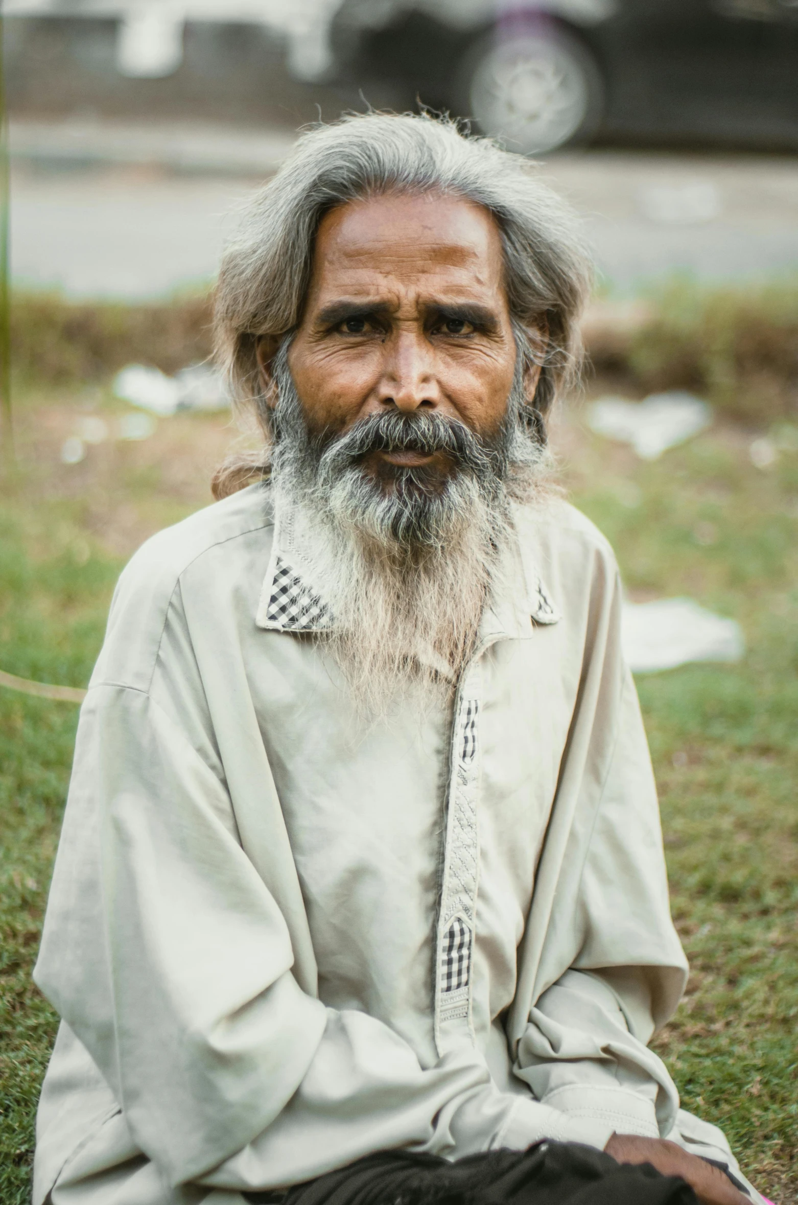 old man sitting on a patch of grass in front of his vehicle