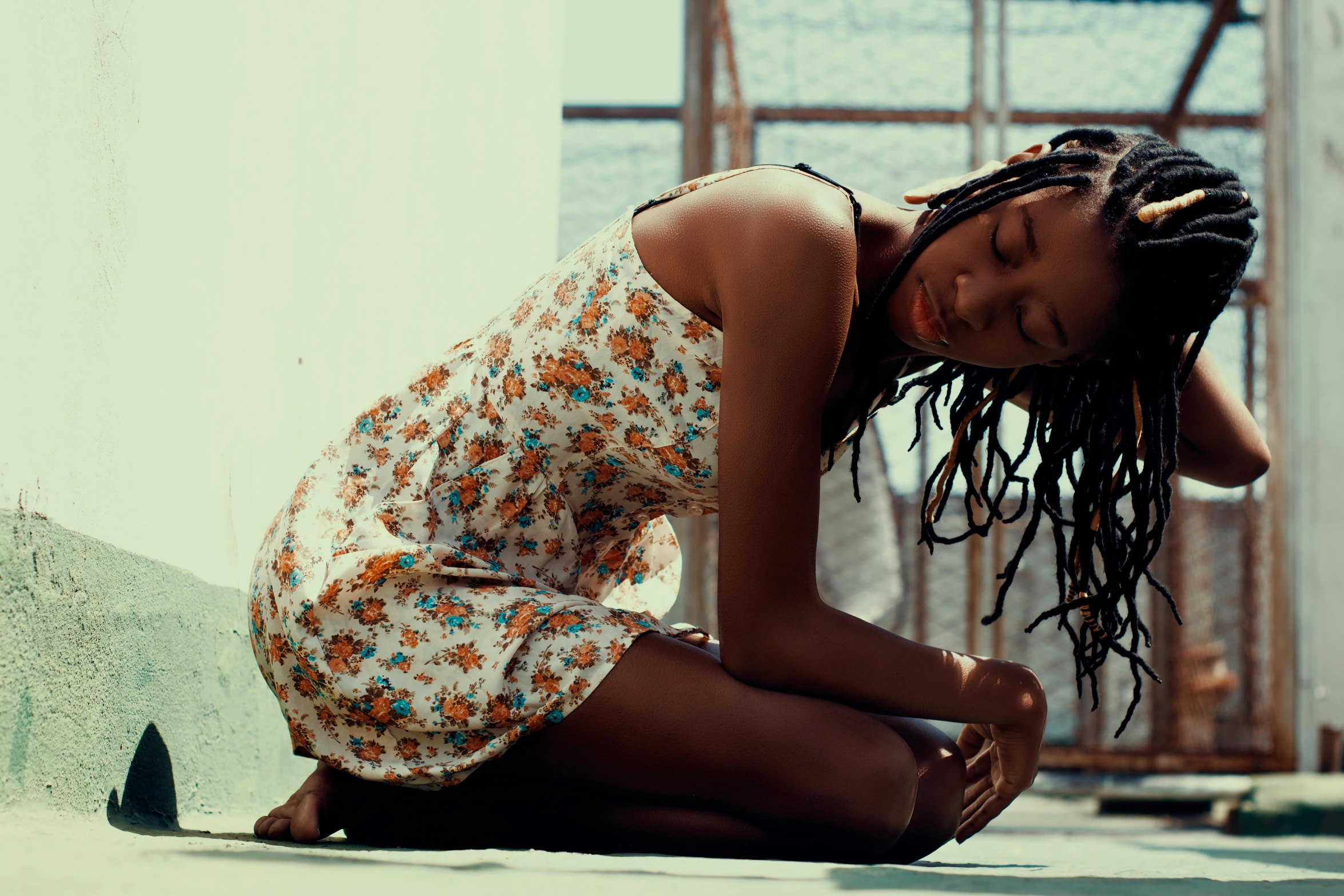 a black woman in an orange and white floral dress is sitting on her stomach