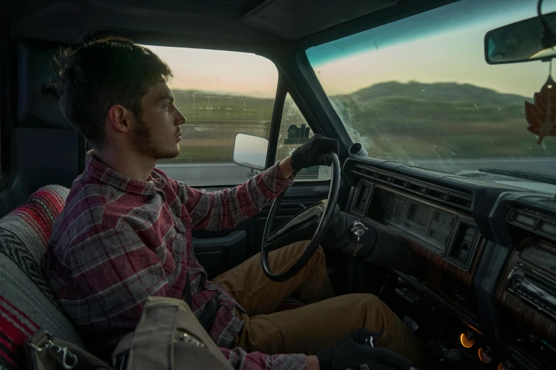 a man sits inside of a truck driving down the road