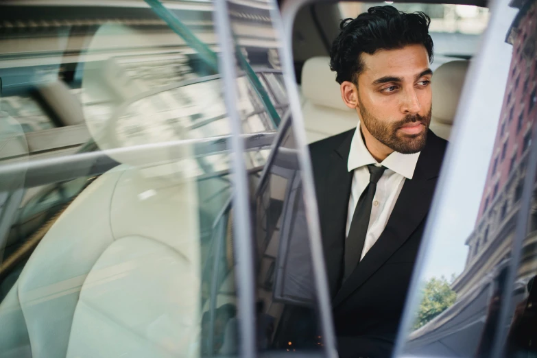 a man in a tuxedo sits inside of a vehicle