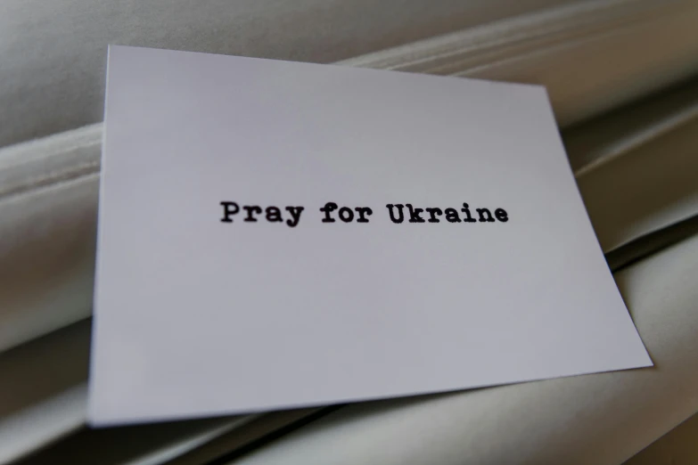 a piece of paper is on top of a white sheet that says pray for ukraine