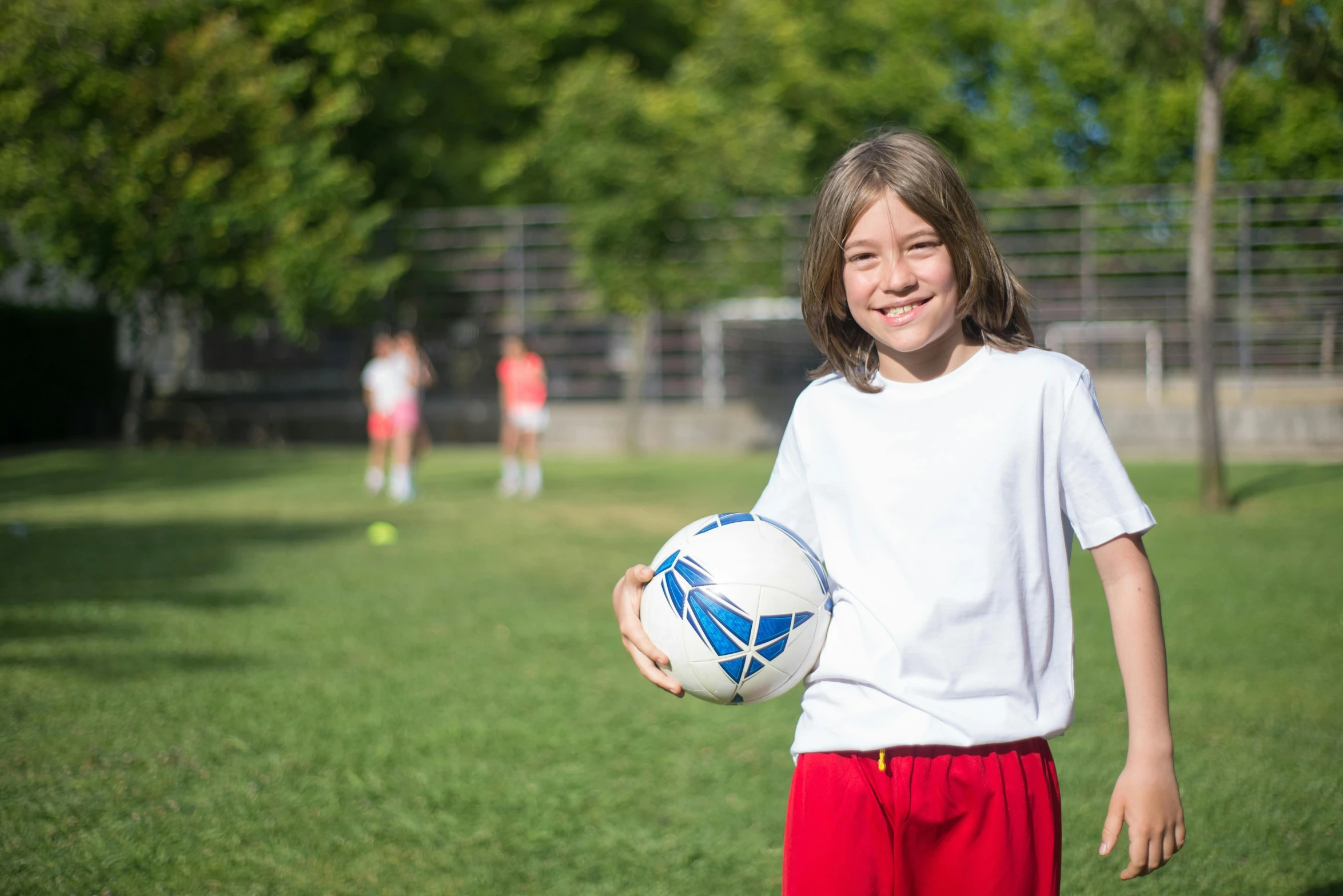 young children standing on green field holding soccer ball