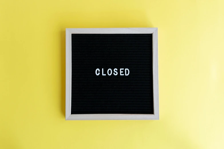 black and white closed sign against a yellow background